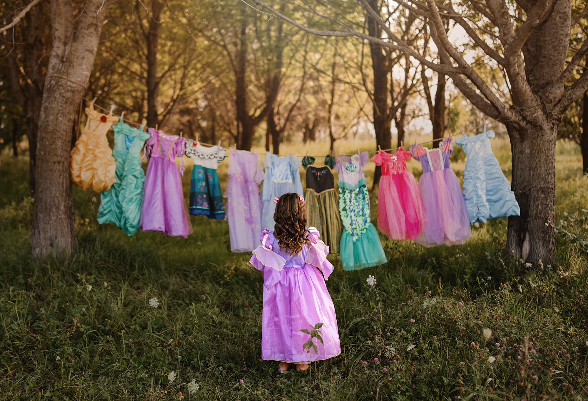 Child in purple dress facing colorful dresses hanging outside.