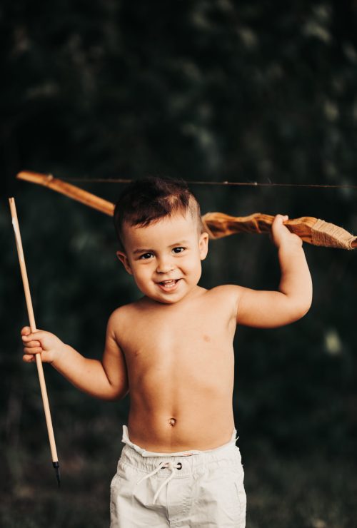 Smiling child holding toy bow and arrow outdoors.
